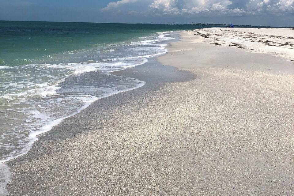 Een strand met kalme golven, een heldere lucht en land in de verte.