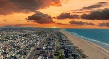 an aerial shot of the vast miles of homes and lush green trees around Huntington Harbour with blue water, majestic mountain ranges, cars driving on the street and powerful clouds at sunset
