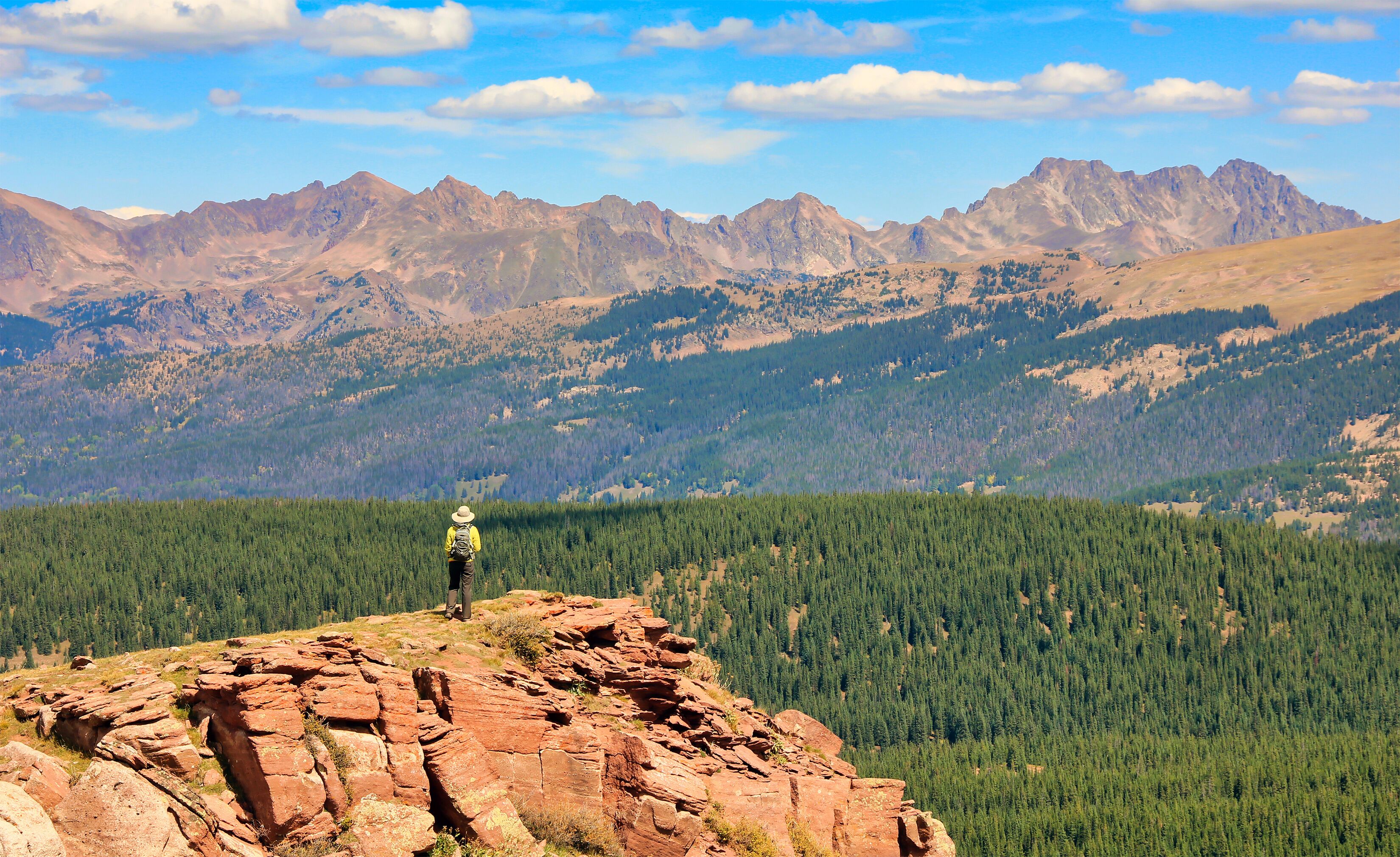 Hiker on top off Shrine Mountain near Colorado's Vail Pass, with a view of the Sawatch Range in the background