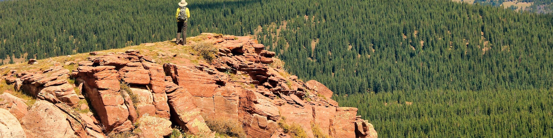 A person standing on a rocky outcrop with a mountainous landscape in the background.