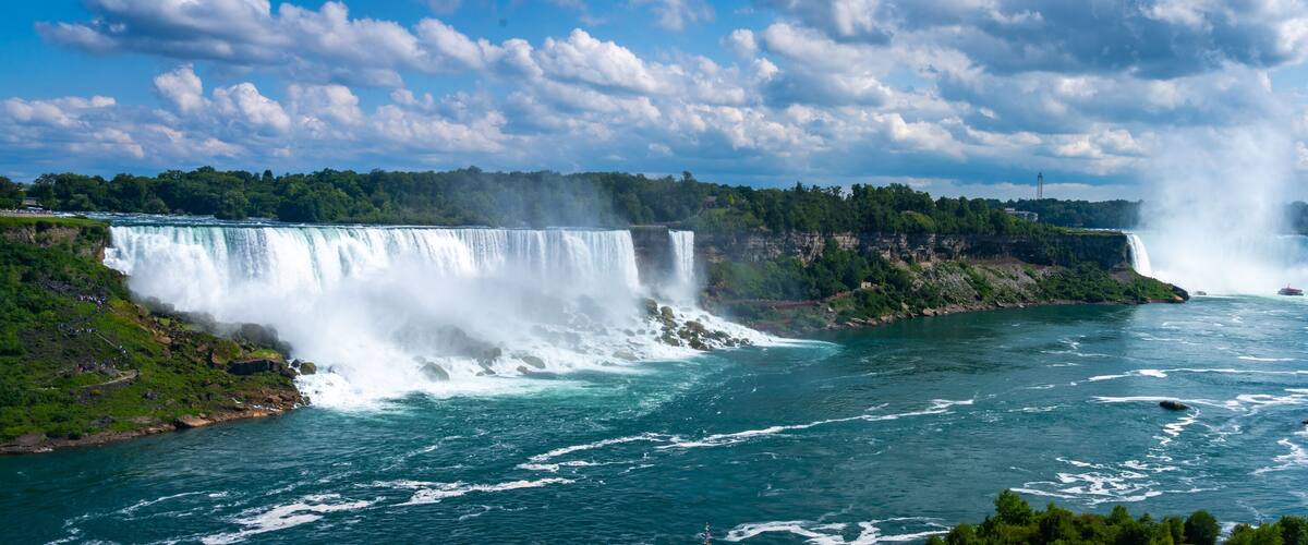 A large waterfall cascading into a river surrounded by lush greenery and cliffs.