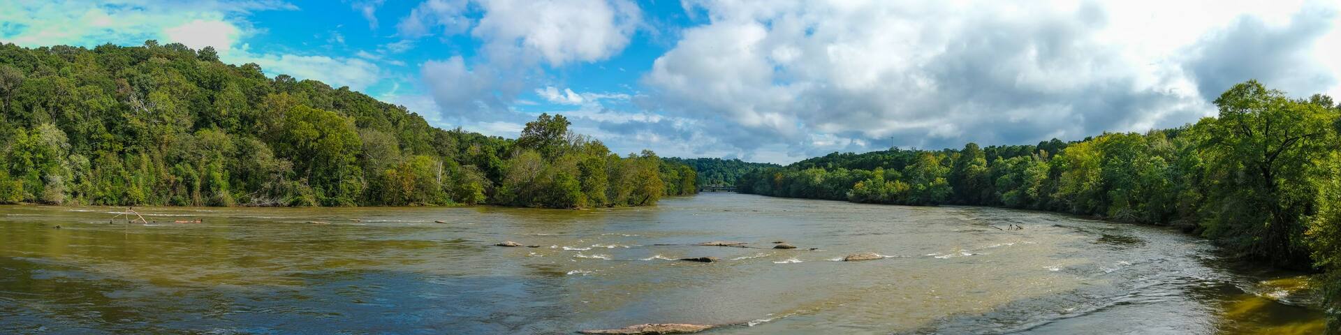 a stunning aerial panoramic shot of the Chattahoochee river surrounded by lush green and autumn colored trees with blue sky and clouds at Cochran Shoals Trail in Marietta USA