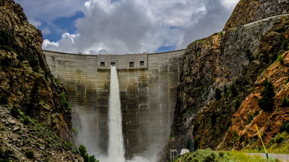 A dam with a waterfall, rocky terrain, and a clear sky.