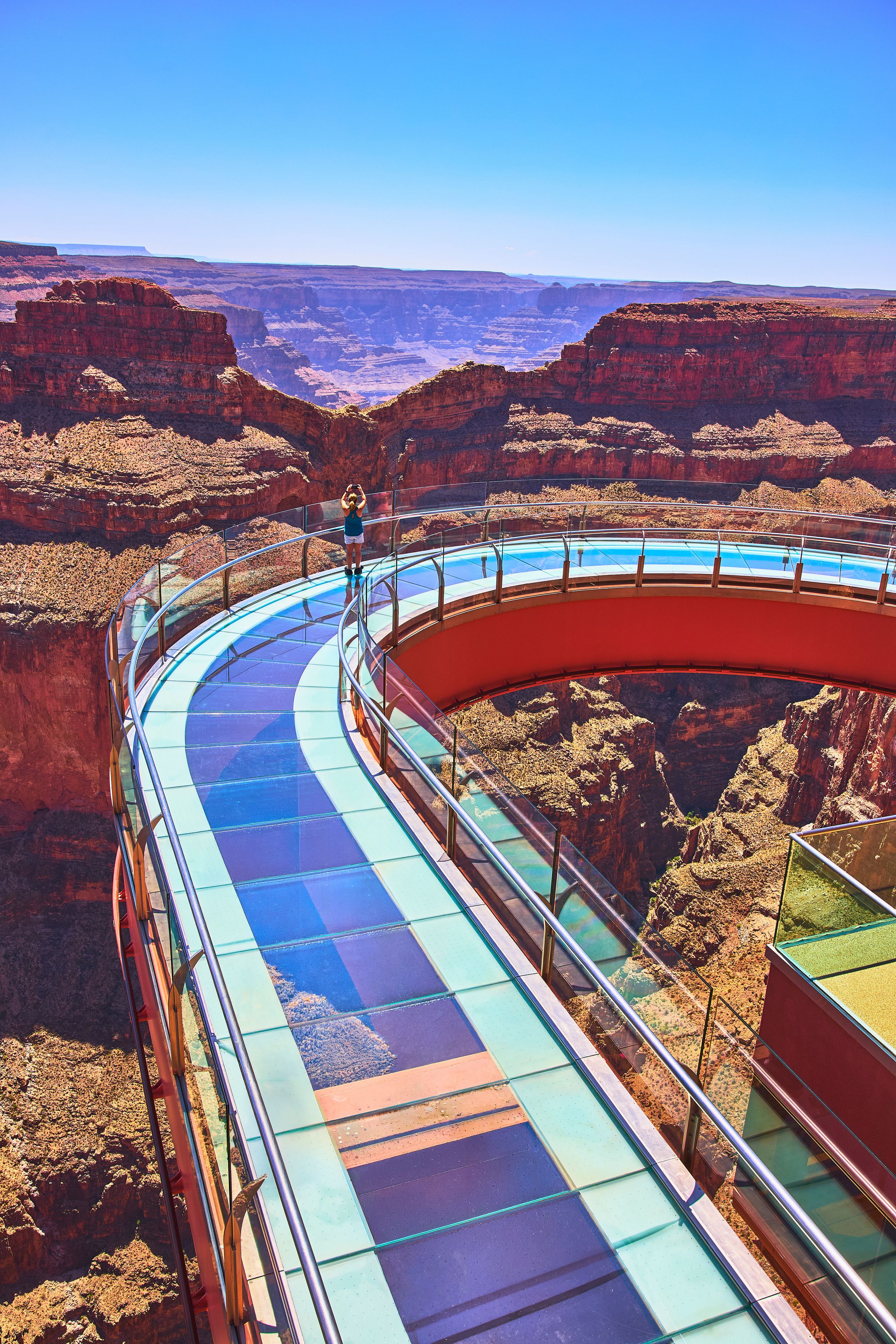 A glass-bottomed walkway curving through a canyon with a clear view of the landscape.