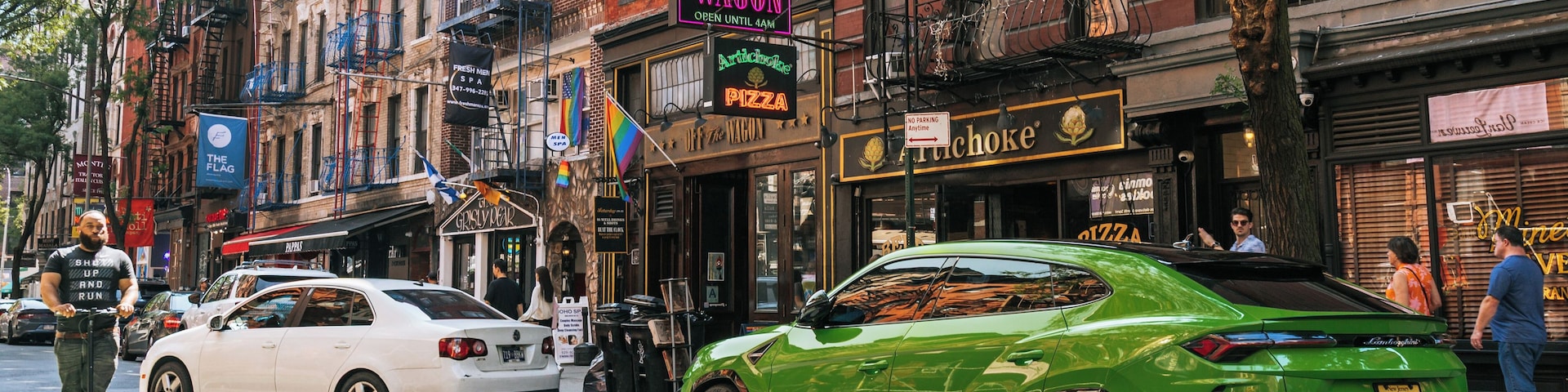 A street with a green sports car, a white car, and a person on a scooter.