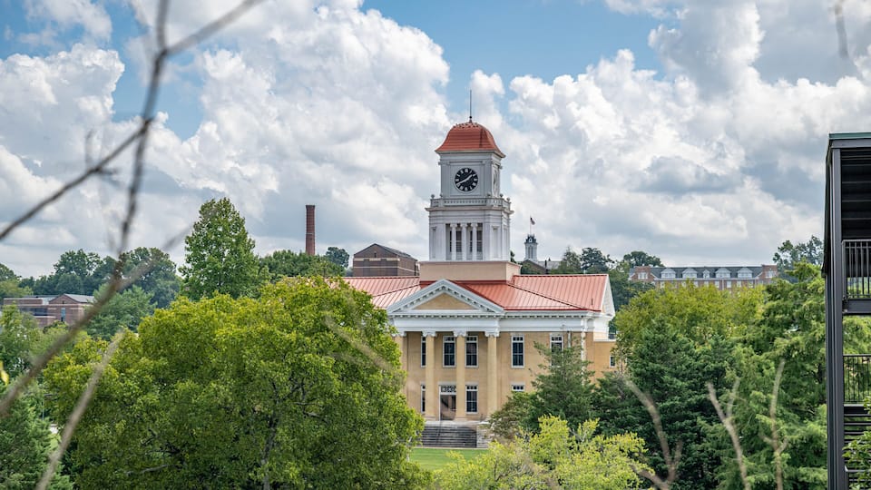 A historic building with a clock tower, surrounded by lush greenery and a partly cloudy sky.