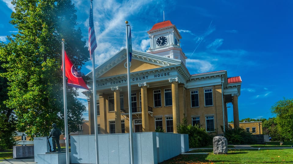 A courthouse with a clock tower, flags, and a statue in front.