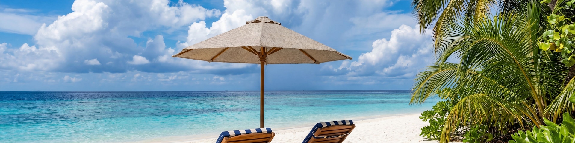 A beach with two wooden lounge chairs and a straw umbrella.