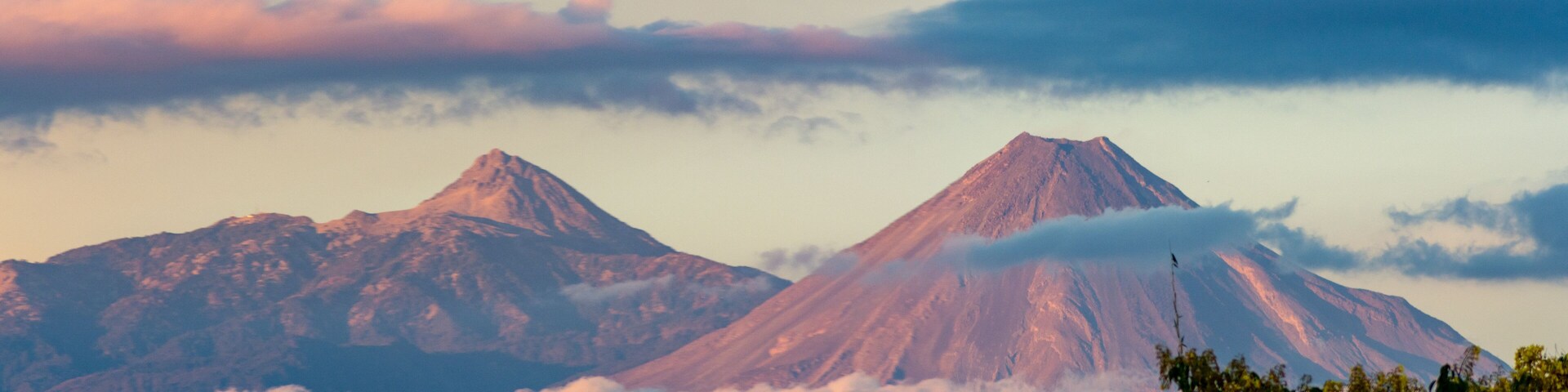 Dos montañas cubiertas de nieve con nubes abajo.