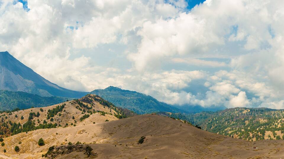 A mountainous landscape with a prominent peak, rolling hills, and a mix of forested areas.