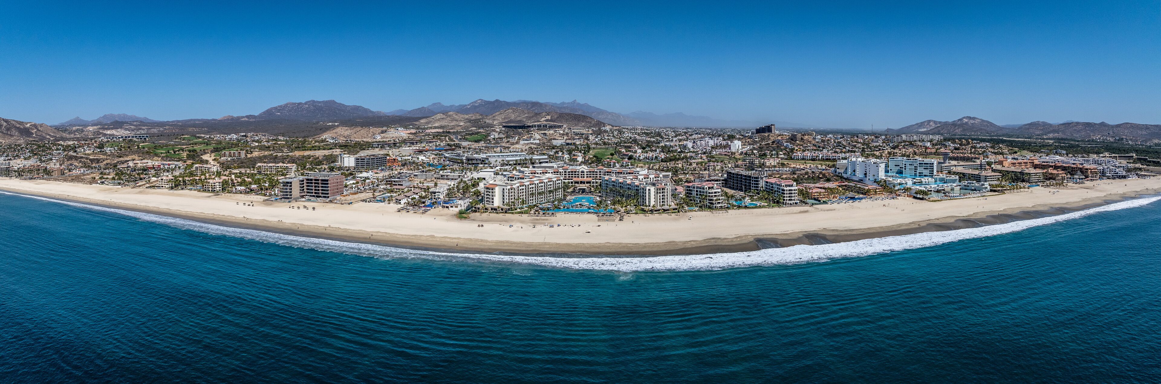 Una ciudad costera con playa, edificios y montañas al fondo.