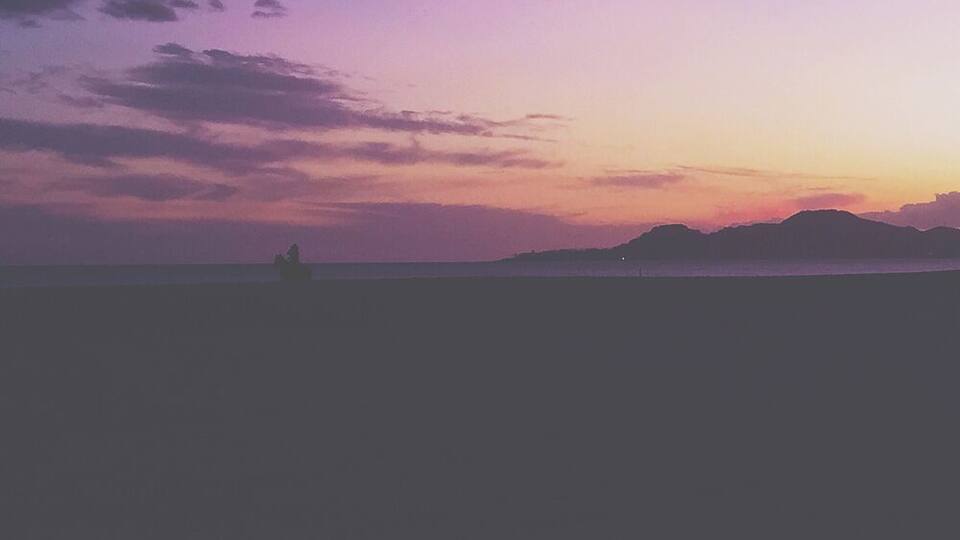 Una playa al atardecer con siluetas de personas y montañas a lo lejos.