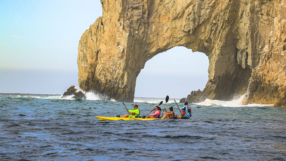 A group kayaking under a natural rock arch formation.