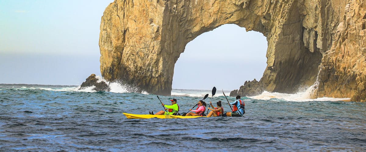 Un grupo practica kayak debajo de una formación rocosa natural en forma de arco.