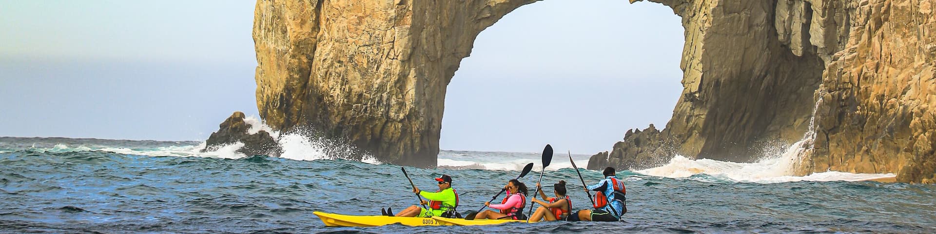 A group kayaking under a natural rock arch formation.