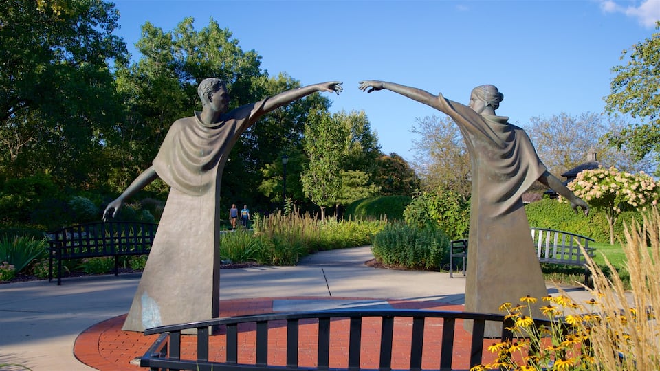 Two bronze statues of figures with outstretched arms in a park with a brick pathway and greenery.