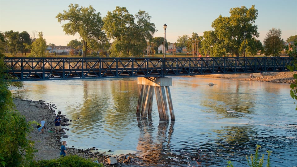 A river with a wooden pier, a bridge, and trees in the background.