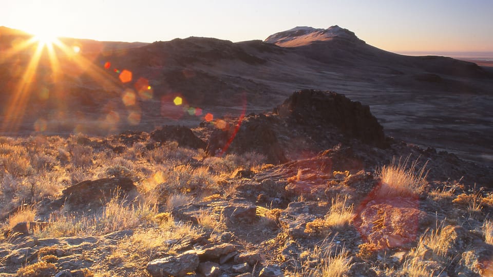 A rocky landscape with a mountain in the background and the sun setting or rising.