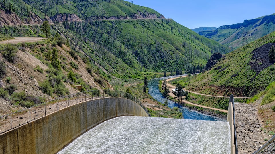 A dam with a river flowing through a valley surrounded by hills.