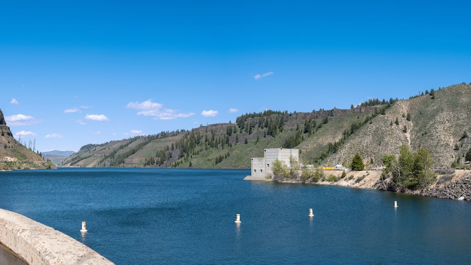 A river with steep cliffs on both sides, a concrete dam, and a clear blue sky.