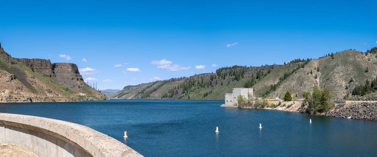 A river with steep cliffs on both sides, a concrete dam, and a clear blue sky.
