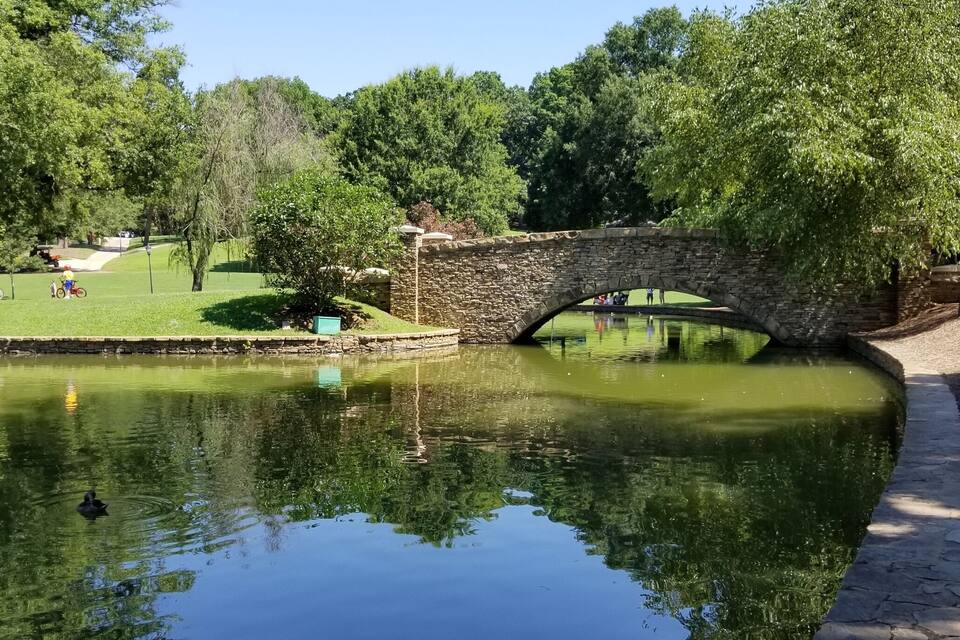 A stone bridge over a pond with ducks swimming.