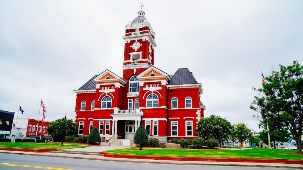 A red courthouse with a clock tower, surrounded by green lawns and trees.