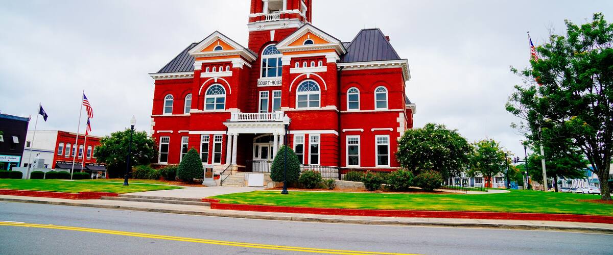 A red courthouse with a clock tower, surrounded by green lawns and trees.