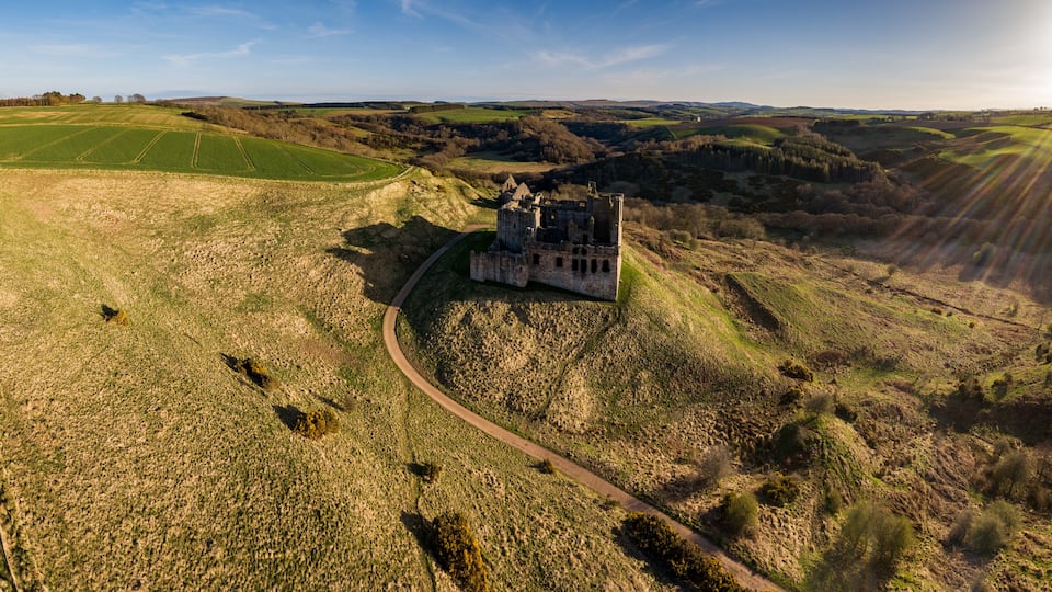 A castle on a hill surrounded by fields and a clear sky.