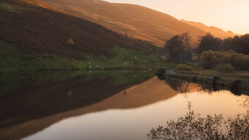 A calm, still peaceful countryside landscape at sunset or sunrise at Glencorse Resevoir in the Pentland Hills Regional Park in Edinburgh, Midlothian, Scotland.