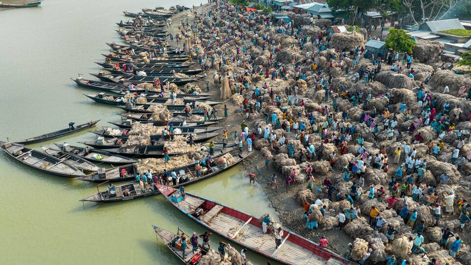 A river with numerous boats and a large crowd of people on the shore.