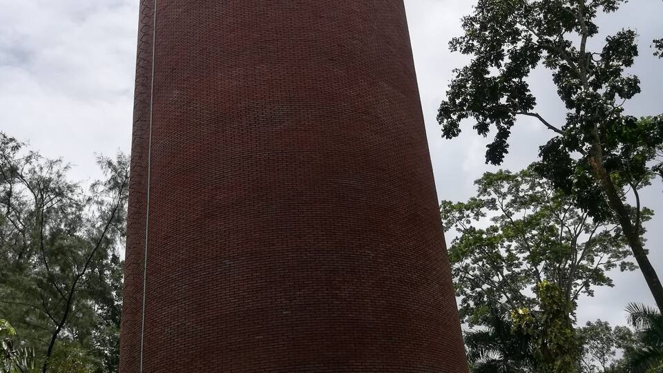 A tall brick tower with a circular pattern on its side, surrounded by lush greenery and trees.
