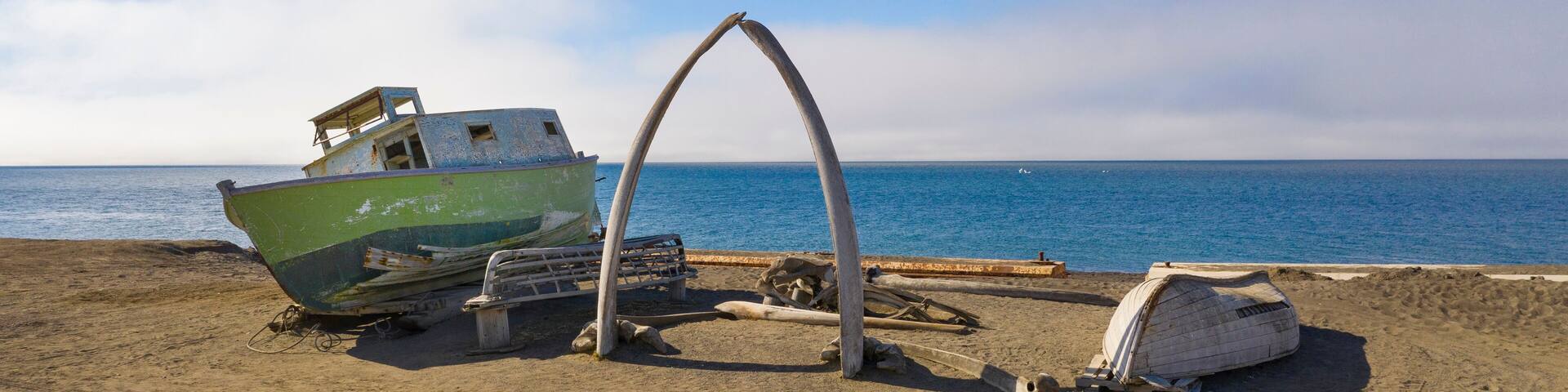 A beach with a green boat, a wooden structure, and a white dome-like object.