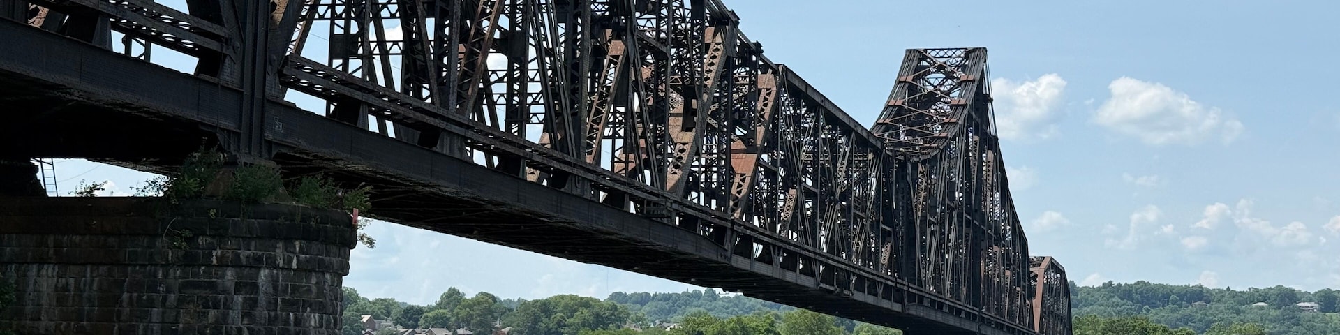 Un puente de acero grande que cruza un río, con abundante vegetación al fondo.