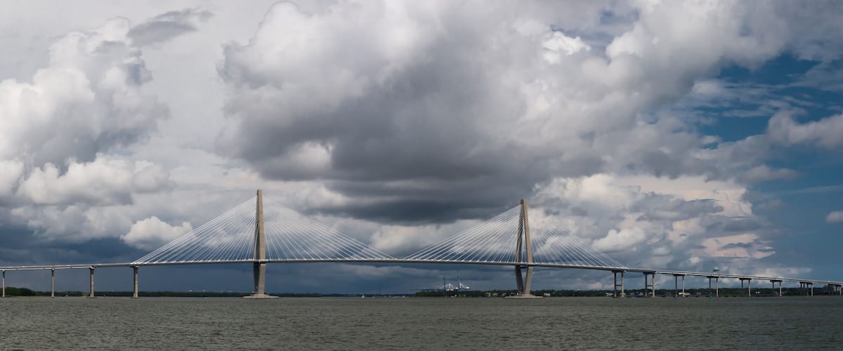 A large suspension bridge over a body of water with a cloudy sky in the background.