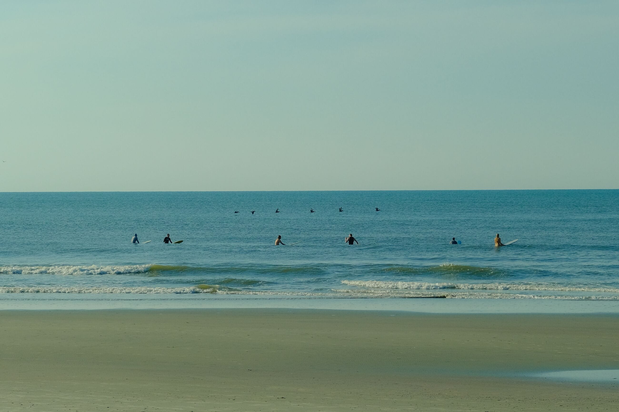 Uma praia com águas calmas e vários surfistas ao longe.