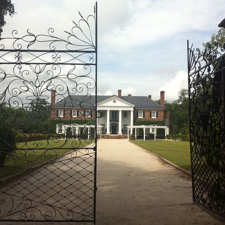 A gated entrance to a large brick house with a white porch and a fountain.