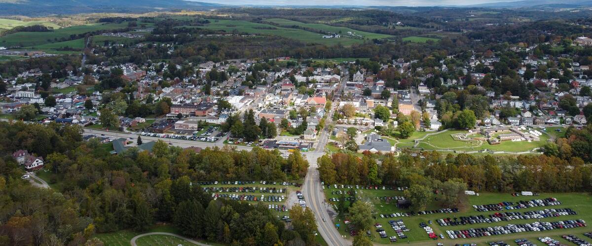 A town with a central road, surrounded by green fields and a mountainous backdrop.