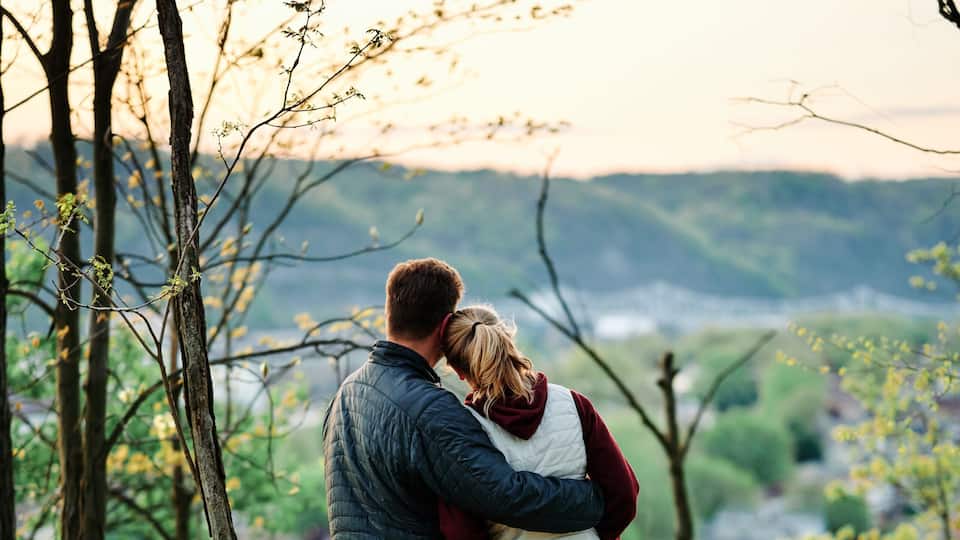A couple embracing in a wooded area with a dog lying on the grass.