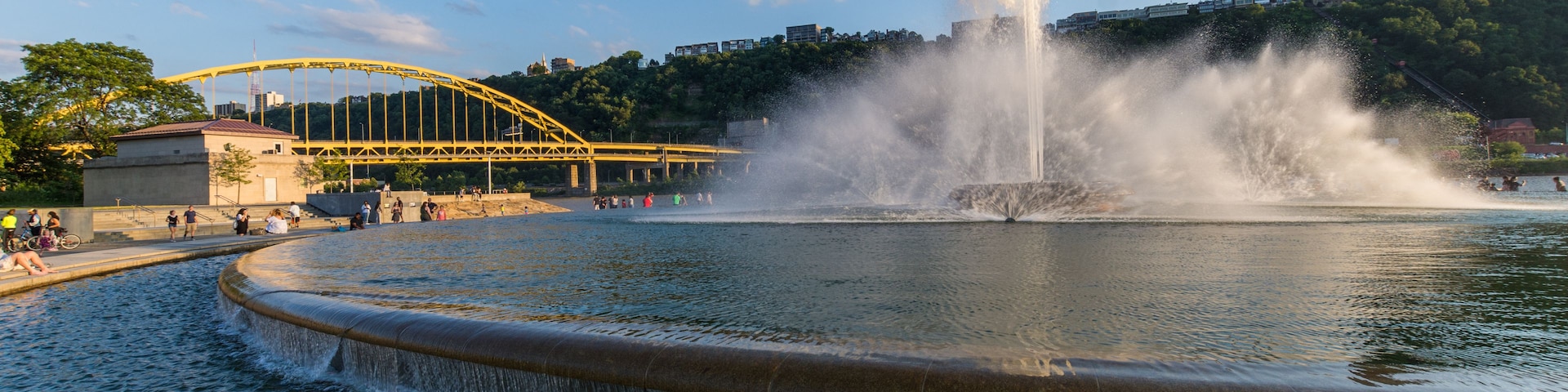 Une fontaine avec des jets d’eau, un pont jaune et une vue sur la ville en arrière-plan.