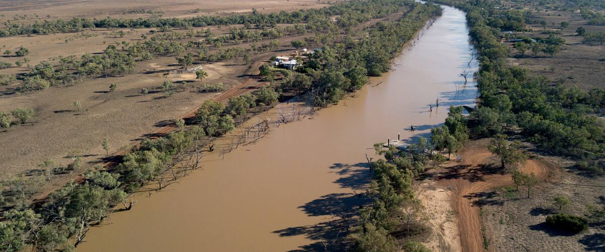 A river winding through a semi-arid landscape with sparse vegetation and a few scattered houses.