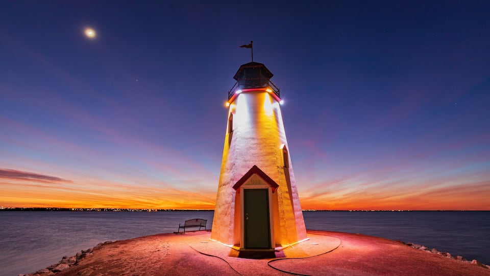 A lighthouse at sunset with a bench nearby.