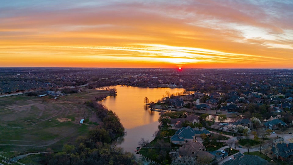A sunset over a river with a residential area and a field.