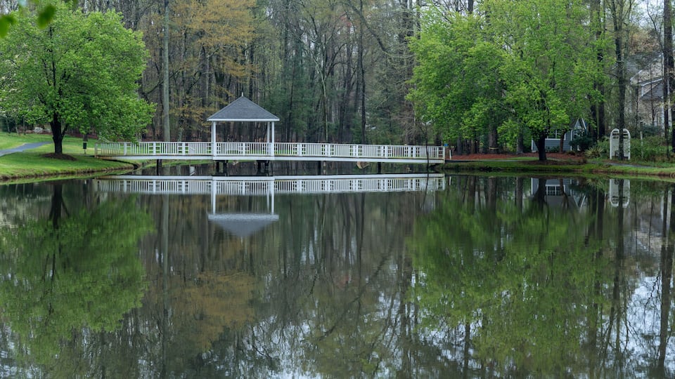 A gazebo by a calm lake surrounded by trees.