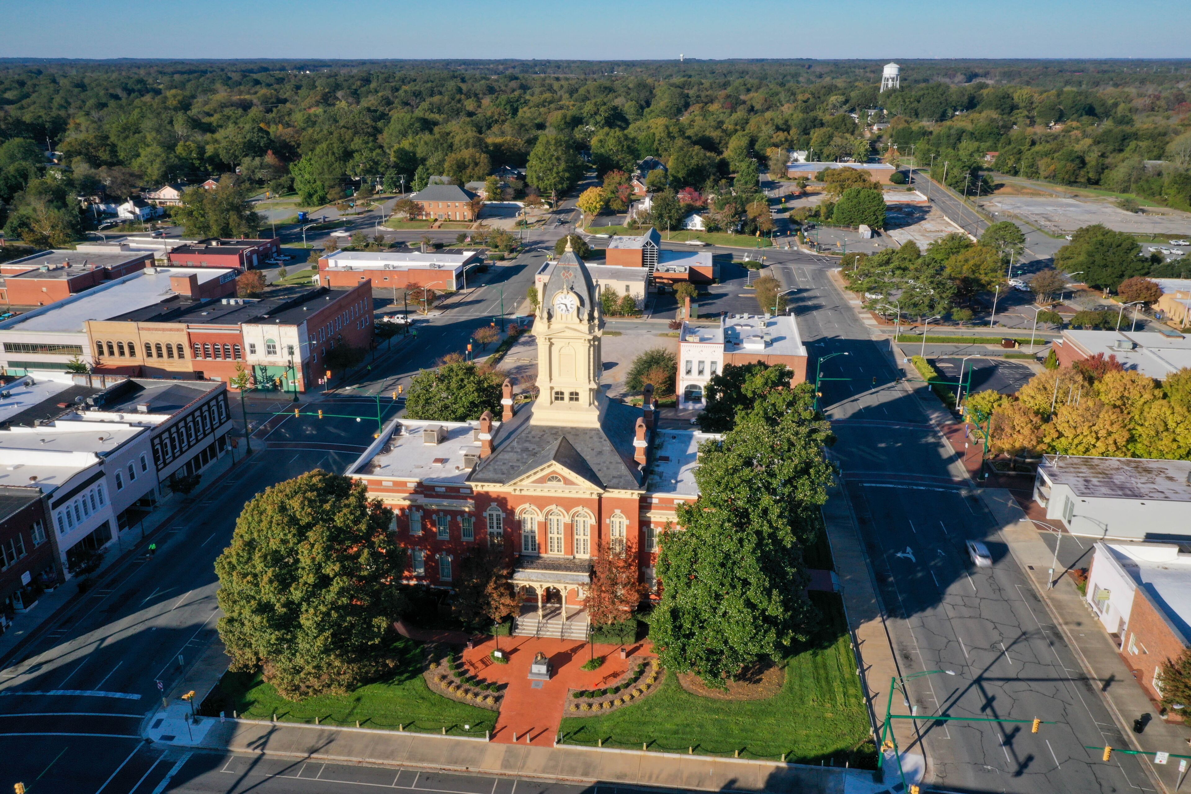 A town square with a prominent clock tower, surrounded by historic buildings and a large green park.