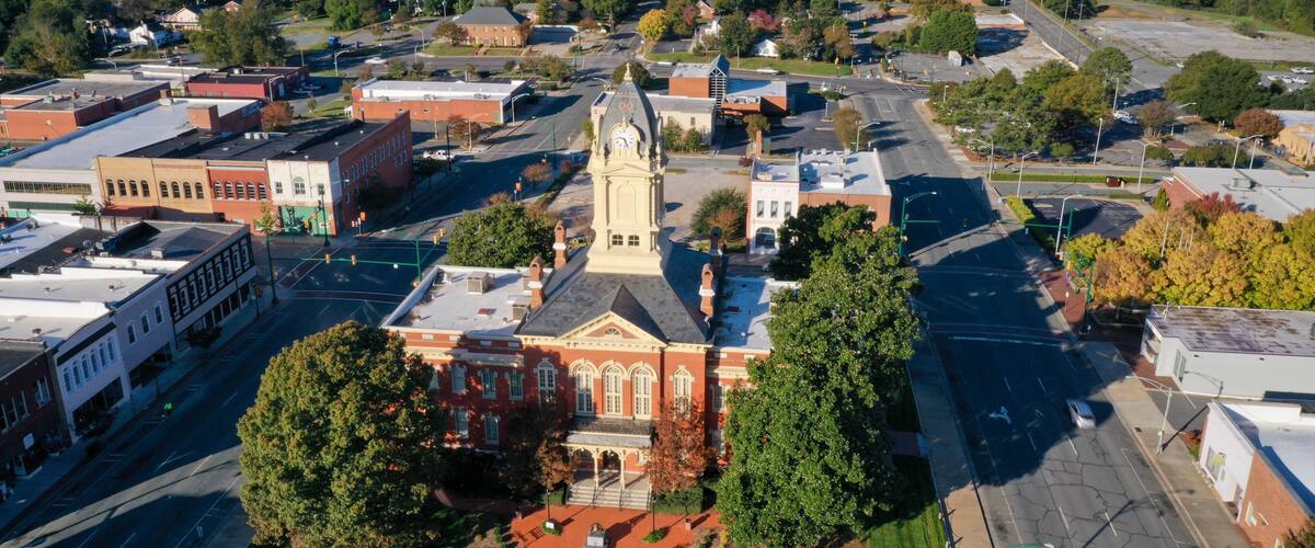 A town square with a prominent clock tower, surrounded by historic buildings and a large green park.