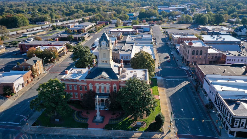 An aerial view of a town with a prominent red building with a clock tower, surrounded by streets and other buildings.