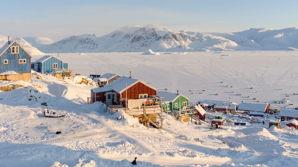 A snow-covered village with buildings and a mountainous backdrop.