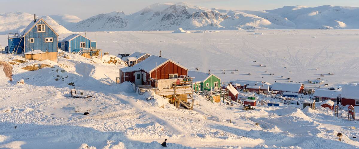 A snow-covered village with buildings and a mountainous backdrop.