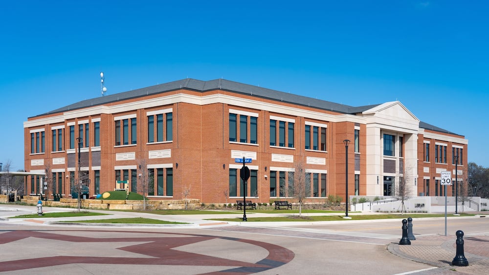 A large brick building with a central entrance, a speed limit sign of 30, and a clear blue sky.